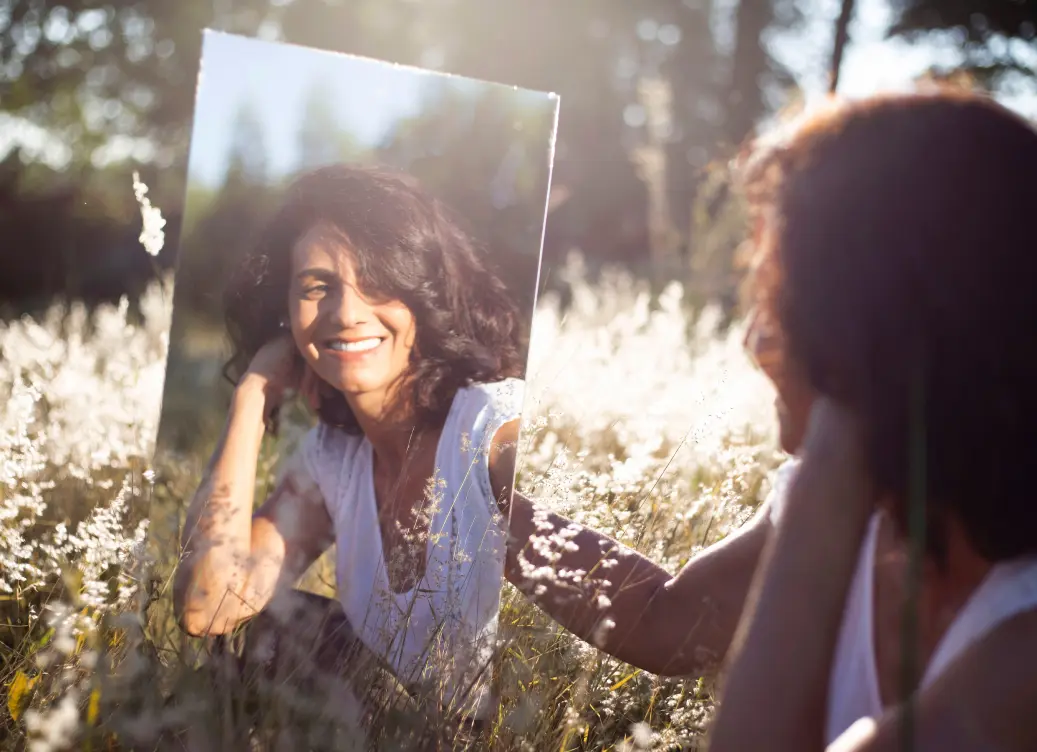 Mujer sonriendo viendose en un espejo entre la flora